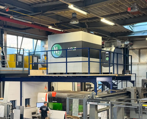In der Mitte des Bildes ist die Valenta Metall Stickstoff Anlage auf einem Zwischenstockwerk in einer Halle mit einer Decke aus Metallkonstruktion und einer Laserschnittanlage auf der Basis