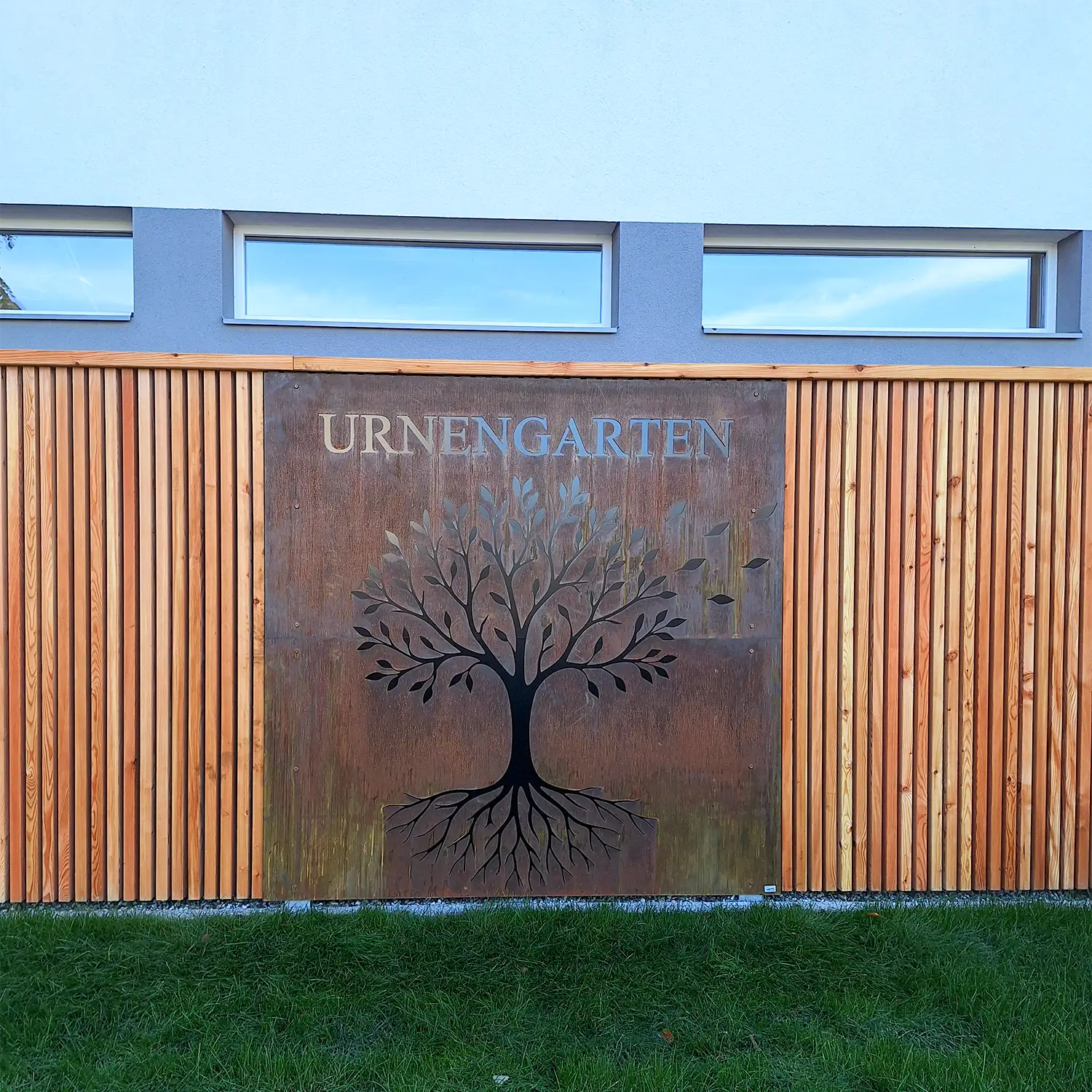 Urnengarten Jochberg, mit einem Laser ausgeschnittener Bauch in einem rostigen Corten-Stahl-Blech. Links und rechts ist eine Wand aus Holzlatten